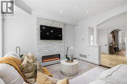 Living space featuring a stone-clad fireplace surround with a linear electric fireplace, recessed lighting, crown molding, and an arched entry - 