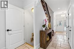 Inviting entryway featuring natural stone tile flooring, a wood-finish staircase with dark banister, recessed lighting, and a front door with decorative glass inserts - 