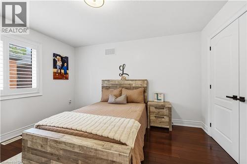 Bedroom featuring dark wood-finish flooring, white walls, and a window with white plantation shutters - 199 Hunter Street W, Hamilton, ON - Indoor Photo Showing Bedroom