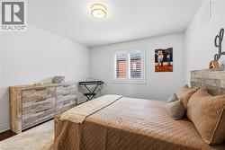 Bedroom featuring a window with white louvered shutters, a wood-finish bed frame, and a complementary wood-finish dresser with dark hardware - 