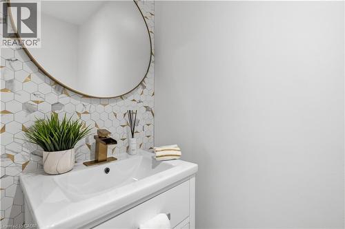 White vanity with integrated sink, brass waterfall faucet, and round brass-framed mirror - 199 Hunter Street W, Hamilton, ON - Indoor Photo Showing Bathroom