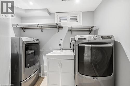 Dedicated utility space featuring a laundry sink with a chrome faucet, white cabinetry, and overhead shelving with a hanging rod - 199 Hunter Street W, Hamilton, ON - Indoor Photo Showing Laundry Room