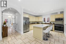 Spacious kitchen featuring light-toned cabinetry, stainless steel appliances, a center island with a stone countertop, and light-toned tile flooring - 