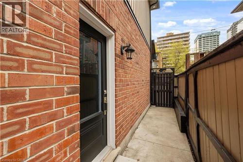 Brick exterior featuring a black entry door with upper glass paneling, an exterior wall lantern, a concrete pathway, and a wooden privacy fence with a gated entry - 199 Hunter Street W, Hamilton, ON - Outdoor With Exterior