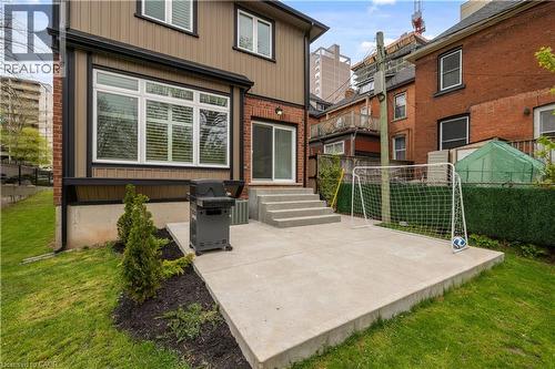 Rear exterior featuring a concrete patio, sliding glass door, and multiple windows with blinds - 199 Hunter Street W, Hamilton, ON - Outdoor