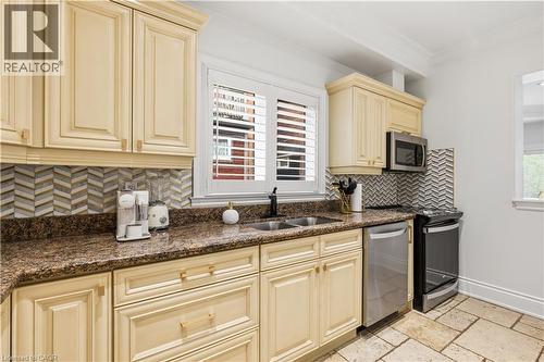 Kitchen featuring cream-colored cabinetry, stone countertops, and a chevron-patterned tile backsplash - 199 Hunter Street W, Hamilton, ON - Indoor Photo Showing Kitchen With Double Sink