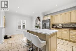 Kitchen featuring a central island with a white countertop, beige cabinetry, stainless steel refrigerator, patterned tile backsplash, and light-toned tile flooring - 