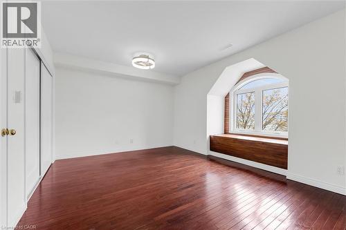 Room featuring rich wood-finish flooring, a large arched window with a built-in wood bench, white painted walls, and a contemporary flush-mount ceiling light - 1389 Lakeshore Road, Burlington, ON - Indoor Photo Showing Other Room
