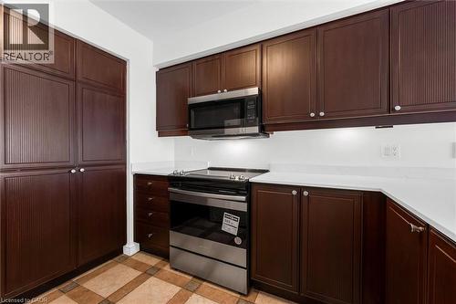 Kitchen featuring dark wood-finish cabinetry, stainless steel appliances, white countertops, and patterned floor tiling - 1389 Lakeshore Road, Burlington, ON - Indoor Photo Showing Kitchen