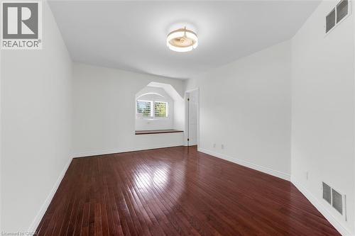 Spacious room featuring rich wood-finish flooring, crisp white walls, and a recessed arched window with plantation shutters - 1389 Lakeshore Road, Burlington, ON - Indoor Photo Showing Other Room
