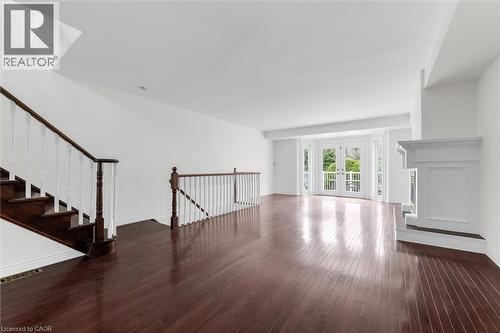 Spacious living area featuring polished wood-finish flooring, a white mantel fireplace, and a striking staircase with dark wood treads and white balusters - 1389 Lakeshore Road, Burlington, ON - Indoor Photo Showing Other Room