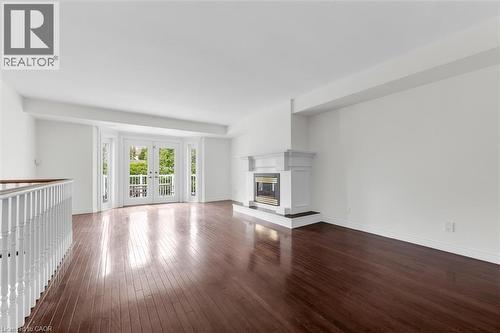 Spacious room featuring rich wood-finish flooring, a contemporary fireplace with a classic mantel, and double French doors opening to a balcony - 1389 Lakeshore Road, Burlington, ON - Indoor With Fireplace