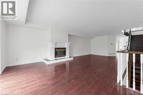 Spacious interior featuring wood-finish flooring throughout, a classic white fireplace with a dark hearth, and a dark wood staircase with white balusters - 1389 Lakeshore Road, Burlington, ON - Indoor With Fireplace