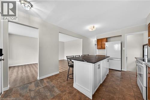 Kitchen featuring a dark stone island with seating, white cabinetry, tile flooring, and a white refrigerator - 34 Avenue Road, Cambridge, ON - Indoor Photo Showing Kitchen