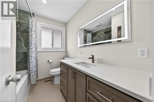 Bathroom featuring an illuminated vanity mirror, a single-basin sink with dark bronze faucet, and a stone-finish countertop - 34 Avenue Road, Cambridge, ON - Indoor Photo Showing Bathroom