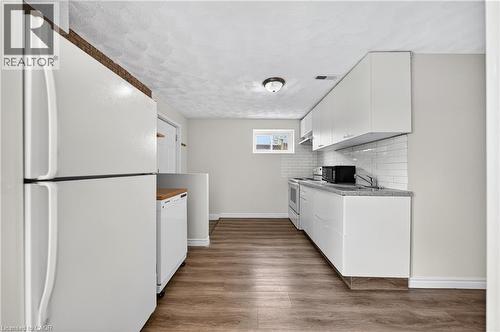Kitchen area featuring wood-finish flooring, white cabinetry, a subway tile backsplash, and a compact window - 34 Avenue Road, Cambridge, ON - Indoor Photo Showing Kitchen