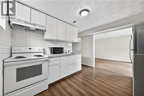 Modern kitchen featuring white cabinetry, subway tile backsplash, a white electric range, and wood-finish flooring - 34 Avenue Road, Cambridge, ON - Indoor Photo Showing Kitchen