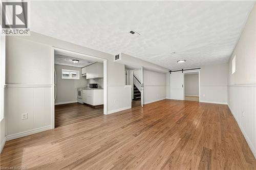Expansive living area featuring wood-finish flooring, wainscoting, a kitchen area with white cabinetry, and a barn door - 34 Avenue Road, Cambridge, ON - Indoor Photo Showing Other Room