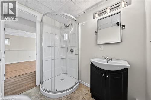 Compact bathroom featuring a curved glass shower enclosure, a dark wood-finish vanity with a white basin sink, and a chrome-framed mirror with overhead lighting - 34 Avenue Road, Cambridge, ON - Indoor Photo Showing Bathroom