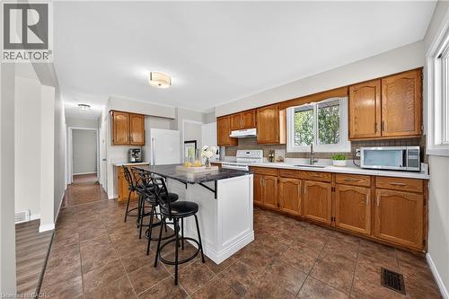 Kitchen featuring an island with seating, extensive wood cabinetry, white countertops, tile flooring, and a large window - 34 Avenue Road, Cambridge, ON - Indoor Photo Showing Kitchen