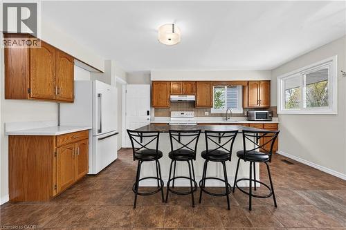 Kitchen featuring wood-finish cabinetry, white countertops, and a central island with an integrated sink and breakfast bar - 34 Avenue Road, Cambridge, ON - Indoor Photo Showing Kitchen With Double Sink