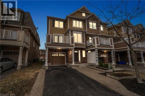 Multi-level townhouse exterior featuring a warm brown and tan color palette, a private balcony with white railings, an integrated single-car garage, and a dedicated driveway - 525 Cavanagh Lane, Milton, ON - Outdoor With Facade
