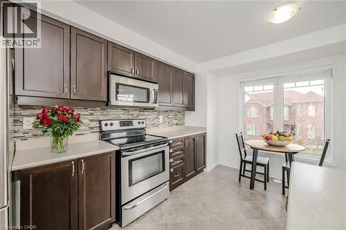 Kitchen featuring dark wood-finish cabinetry, stainless steel appliances, a mosaic tile backsplash, and light-toned countertops - 525 Cavanagh Lane, Milton, ON - Indoor Photo Showing Kitchen With Upgraded Kitchen