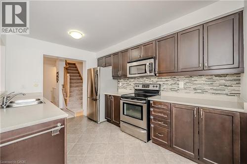 Kitchen featuring dark wood-finish cabinetry, stainless steel appliances, light-toned countertops, and a mosaic tile backsplash - 525 Cavanagh Lane, Milton, ON - Indoor Photo Showing Kitchen With Double Sink