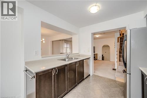 Kitchen featuring neutral-toned tile flooring, light-colored countertops, dark wood-finish cabinetry, a double basin sink, and a stainless steel dishwasher - 525 Cavanagh Lane, Milton, ON - Indoor Photo Showing Kitchen With Double Sink