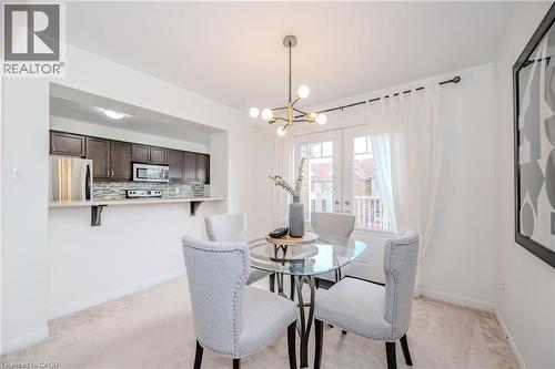 Dining area featuring a contemporary chandelier, light carpeting, and a glass-top table - 525 Cavanagh Lane, Milton, ON - Indoor Photo Showing Dining Room