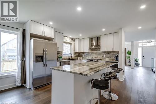 Contemporary kitchen featuring a large central island with seating, stainless steel appliances, white cabinetry, and a stone backsplash - 29 Wiltshire Place, Ancaster, ON - Indoor Photo Showing Kitchen With Upgraded Kitchen