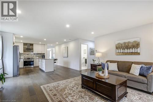 Open-concept living area featuring wood-finish flooring, recessed lighting, and a white kitchen with stainless steel appliances, granite countertops, and a central island - 29 Wiltshire Place, Ancaster, ON - Indoor Photo Showing Living Room