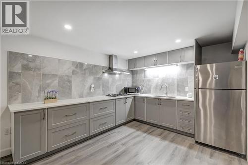 Contemporary kitchen featuring L-shaped gray cabinetry, stainless steel appliances, light-toned countertops, and a gray tile backsplash - 29 Wiltshire Place, Ancaster, ON - Indoor Photo Showing Kitchen With Upgraded Kitchen