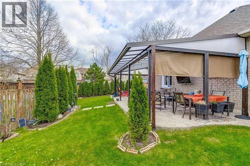Expansive backyard featuring a covered patio with privacy screens, brick exterior, manicured lawn, stone pathway, and mature evergreen plantings - 29 Wiltshire Place, Ancaster, ON - Outdoor