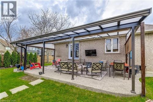 Expansive concrete patio featuring a metal-framed pergola with a translucent roof, a mounted outdoor television, and string lighting - 29 Wiltshire Place, Ancaster, ON - Outdoor