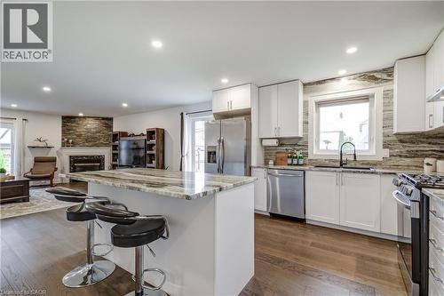 Open-concept kitchen featuring an island with a stone countertop, white cabinetry, stainless steel appliances, and wood-finish flooring - 29 Wiltshire Place, Ancaster, ON - Indoor Photo Showing Kitchen With Upgraded Kitchen