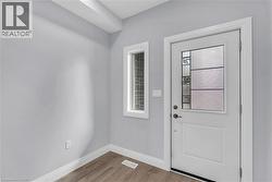 Entryway featuring a white door with decorative glass inserts, a vertical transom window, light gray walls, white baseboards, and wood-finish flooring - 