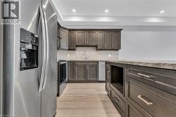 Modern kitchen featuring dark wood-finish cabinetry, stainless steel appliances, speckled stone countertops, a coordinating backsplash, and recessed lighting - 
