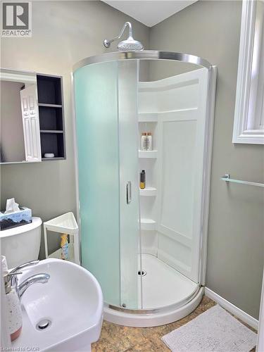 Corner shower enclosure with curved frosted glass doors, white shower pan, integrated shelving, and a chrome shower head - 16 Forest Hill Road, St. Catharines, ON - Indoor Photo Showing Bathroom