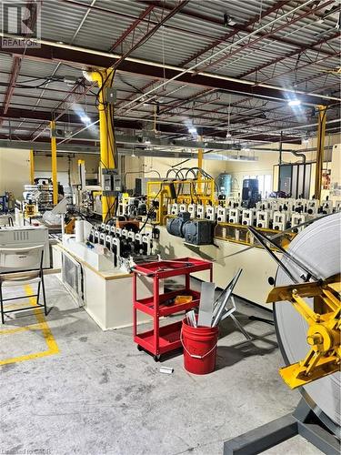 Industrial space featuring high ceilings with exposed structural beams, fluorescent lighting, concrete flooring with yellow safety markings, and large-scale manufacturing equipment - 550 Parkside Drive Unit# A13-16, Waterloo, ON 