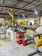 Industrial space featuring high ceilings with exposed structural beams, fluorescent lighting, concrete flooring with yellow safety markings, and large-scale manufacturing equipment - 