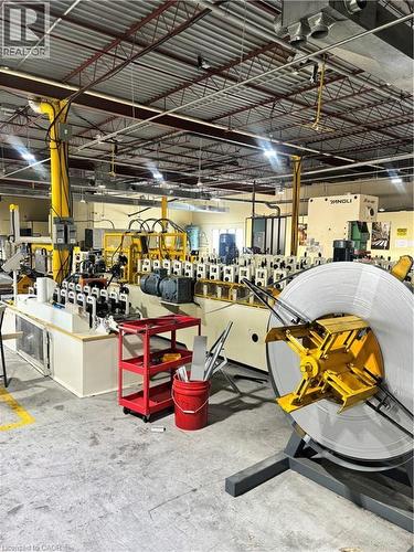 Industrial workspace featuring a metal roll forming line, exposed structural ceiling, integrated overhead lighting, concrete flooring, and yellow safety stanchions - 550 Parkside Drive Unit# A13-16, Waterloo, ON 