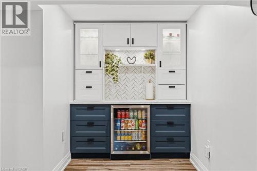 Built-in beverage station featuring white upper cabinetry with glass-front accents, contrasting blue lower cabinetry, a white countertop, and a tiled backsplash - 120 Elgin Crescent, Waterloo, ON - Indoor Photo Showing Other Room