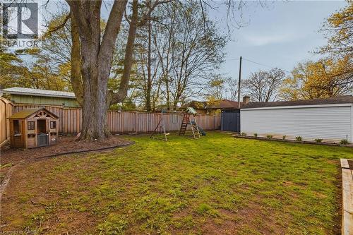 Spacious backyard featuring a large mature tree, wood privacy fencing, a manicured lawn area, and a white siding garage structure with dark gray doors - 120 Elgin Crescent, Waterloo, ON - Outdoor