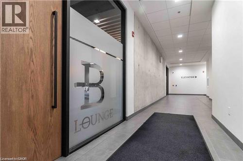 Frosted glass partition with ""Lounge"" branding, wood-finish door with a long black pull handle, concrete accent wall, recessed ceiling lighting, and grey tile flooring - 251 Northfield Drive E Unit# 406, Waterloo, ON - Indoor Photo Showing Other Room