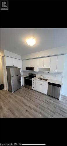 Contemporary kitchen featuring white cabinetry, stainless steel appliances, light-toned countertops, and wood-finish flooring - 251 Northfield Drive E Unit# 406, Waterloo, ON - Indoor Photo Showing Kitchen With Double Sink