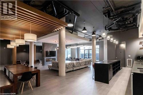 Spacious common area featuring wood-slat ceiling accents, integrated wall-mounted fireplace, exposed ceiling ductwork, dark gray walls, and large format tile flooring - 251 Northfield Drive E Unit# 406, Waterloo, ON - Indoor