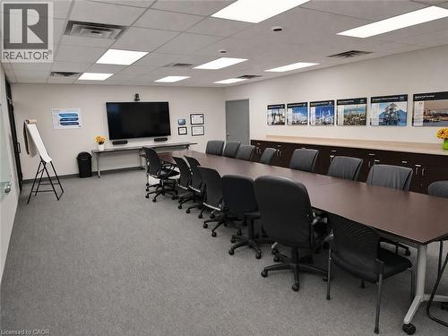 Conference room featuring a long rectangular table, built-in cabinetry with a light wood-finish countertop, a large wall-mounted display, and gray carpet flooring - 920 Sheldon Court, Burlington, ON 
