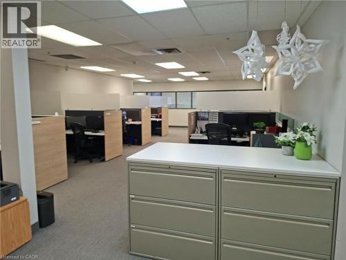 Open-plan office area featuring multiple cubicle workstations with wood-finish dividers, grey carpeted flooring, and acoustic tile ceilings with recessed lighting - 920 Sheldon Court, Burlington, ON 