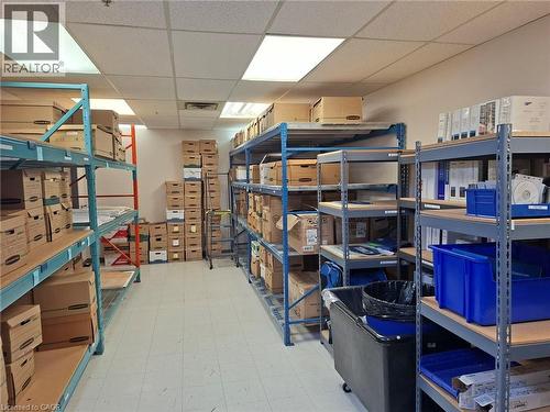 Storage room with suspended ceiling tiles, fluorescent lighting, vinyl tile flooring, and multiple metal shelving units - 920 Sheldon Court, Burlington, ON 